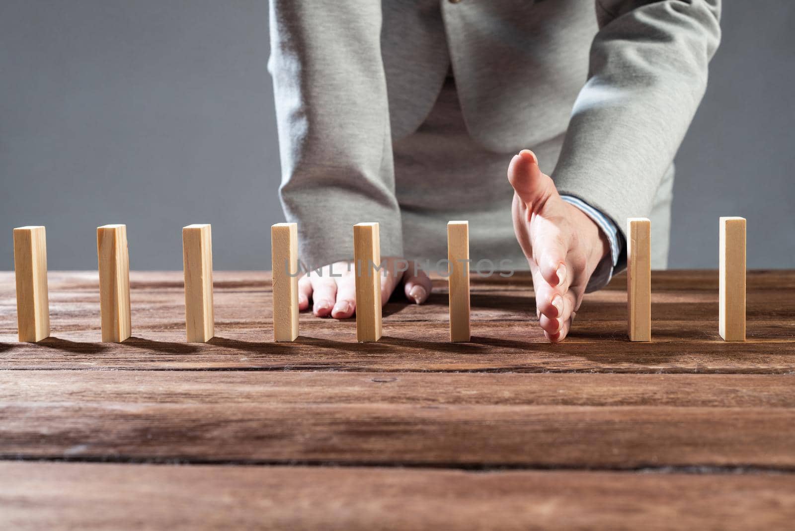 Businesswoman protecting dominoes from falling on wooden desk. Business assistance and leadership in crisis. Operative business solution and stabilization of situation. Professional risk management