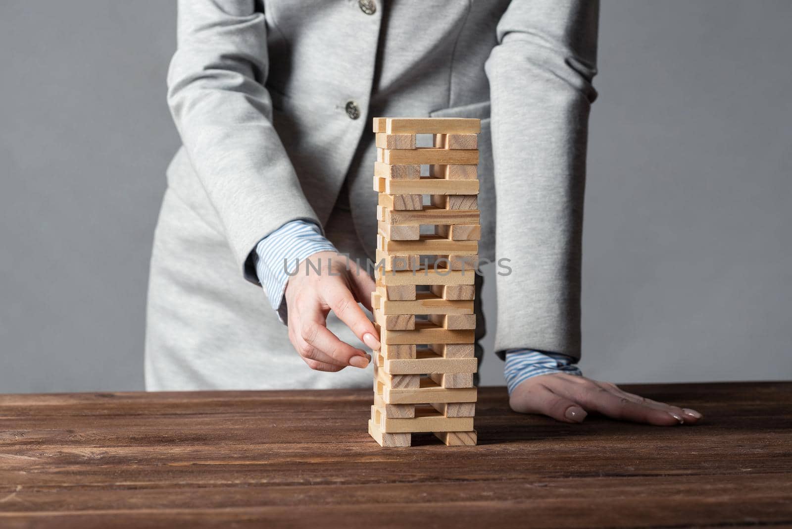 Businesswoman removing wooden block from tower on table. Management of risks concept with wooden boxes game. Business development and assistance. New challenge and leadership motivation.