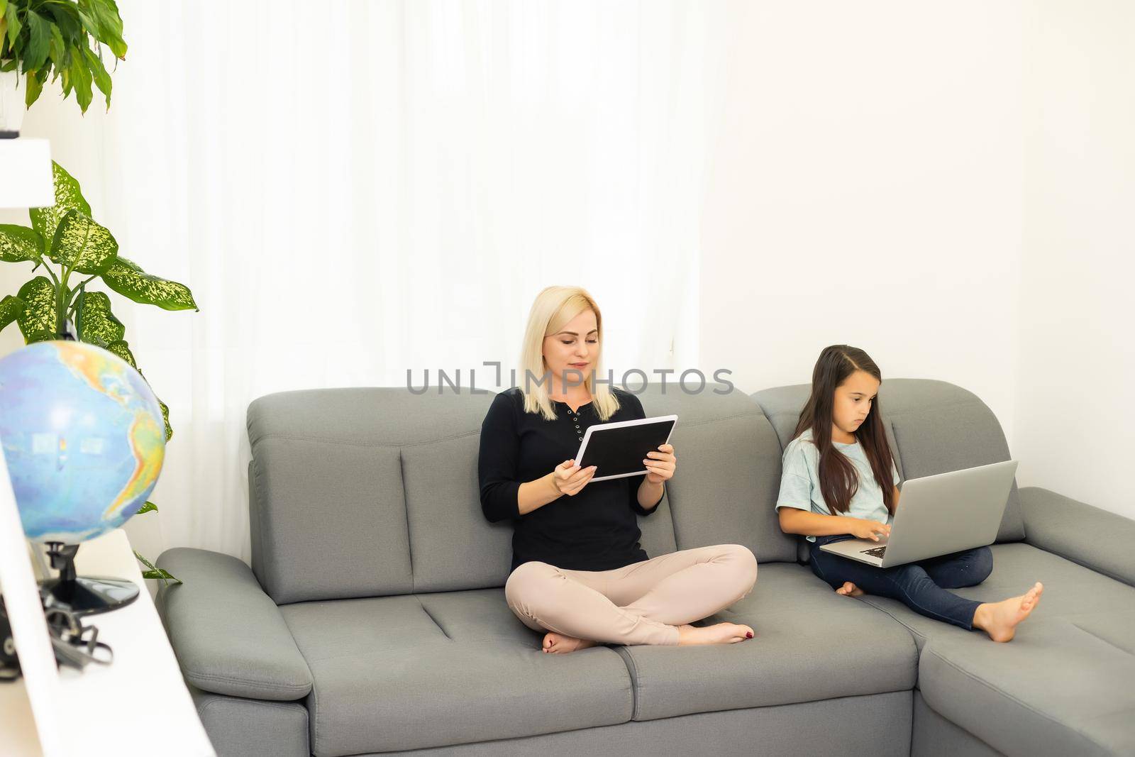 mother works on tablet online and daughter doing homework with a tablet by Andelov13