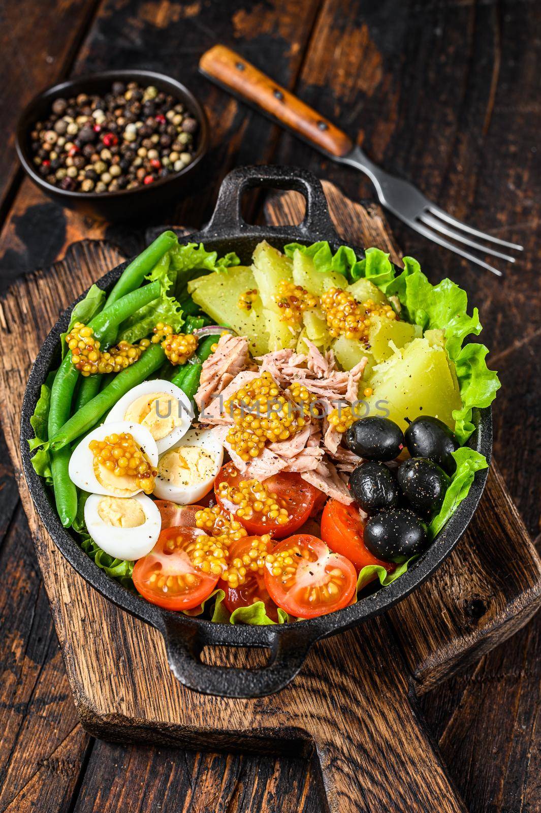 Nicoise salad with tuna, cherry tomatoes, olives, green beans, cucumber, soft boiled eggs and potato. Dark wooden background. top view.