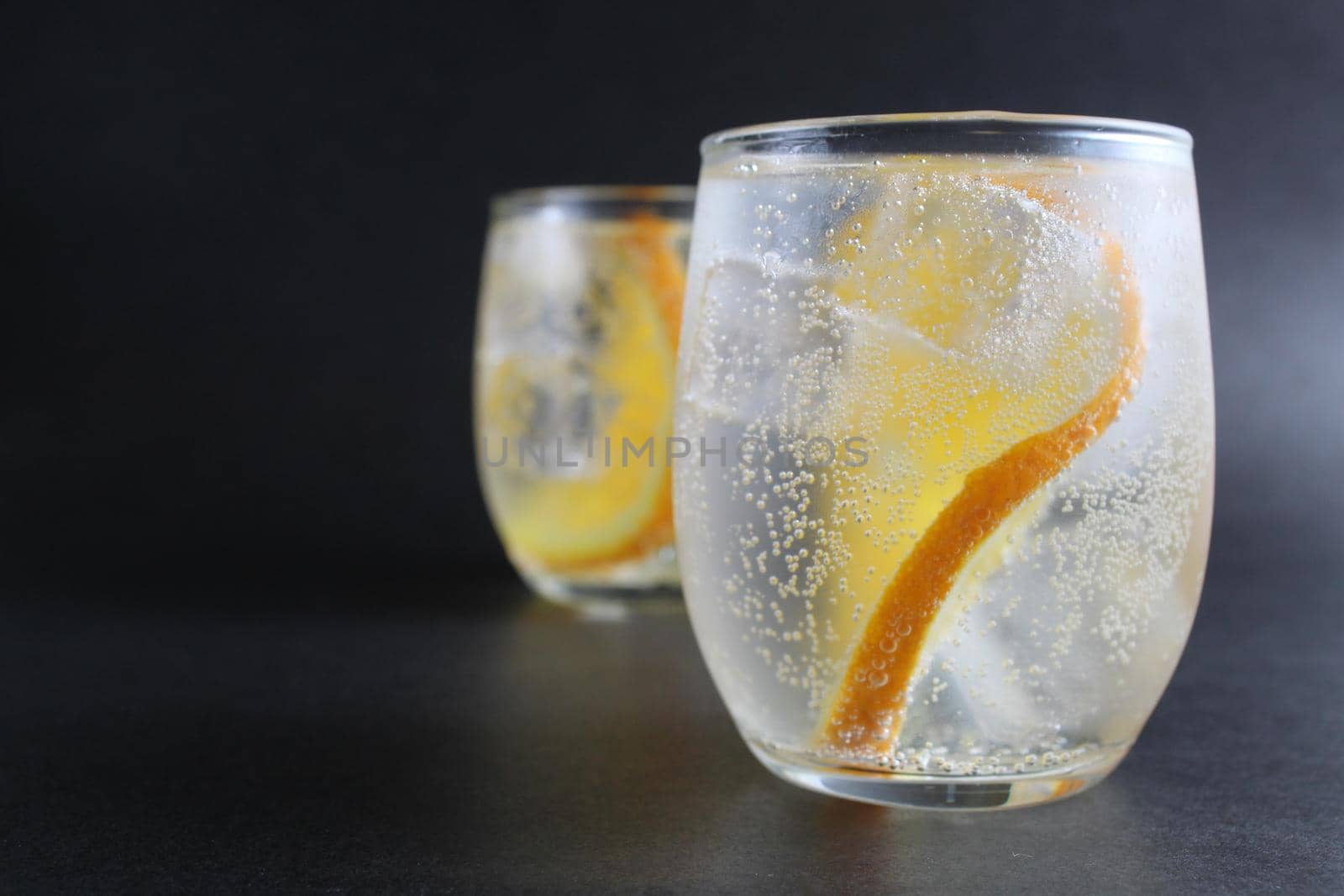 lemonade with orange and ice in a glass on a black background next to lies ice and orange. Summer drink on a black background by Shoba