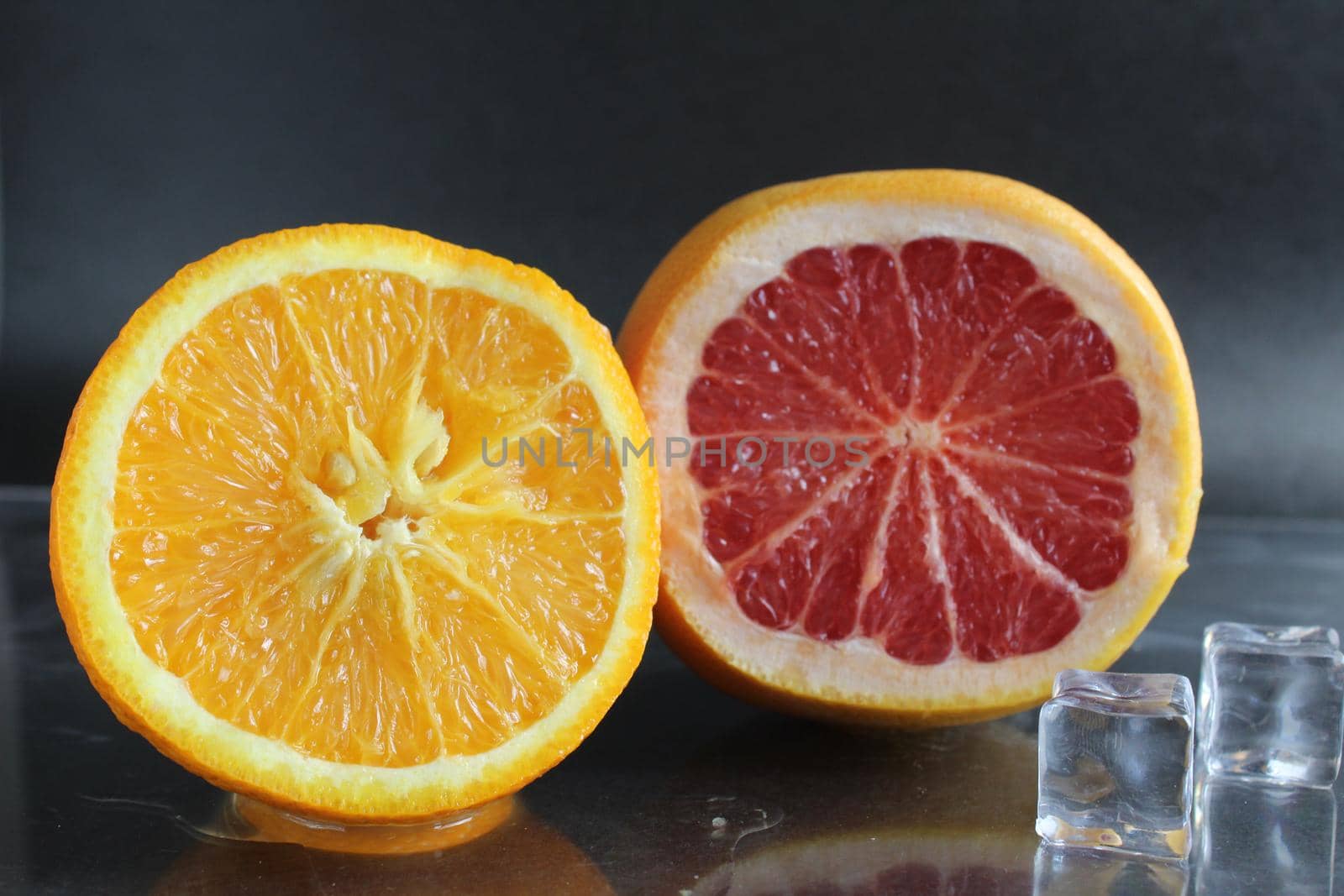 orange and grapefruit in the cut lie next to ice cubes on a black background. Fruit for lemonade. citrus.