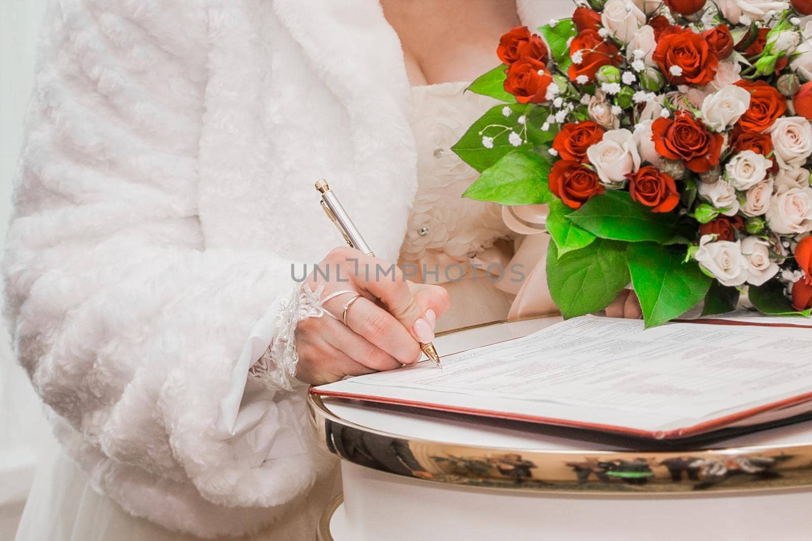 Bride's hand puts signature pen on consent marriage at wedding close-up.