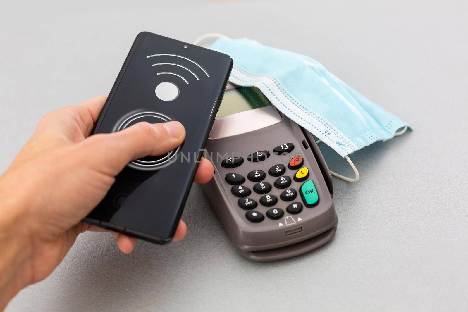 A POS with medical mask waiting for a contactless Nfc payment of groceries on a gray background. Nfc pay. Covid pay. Safe pay.