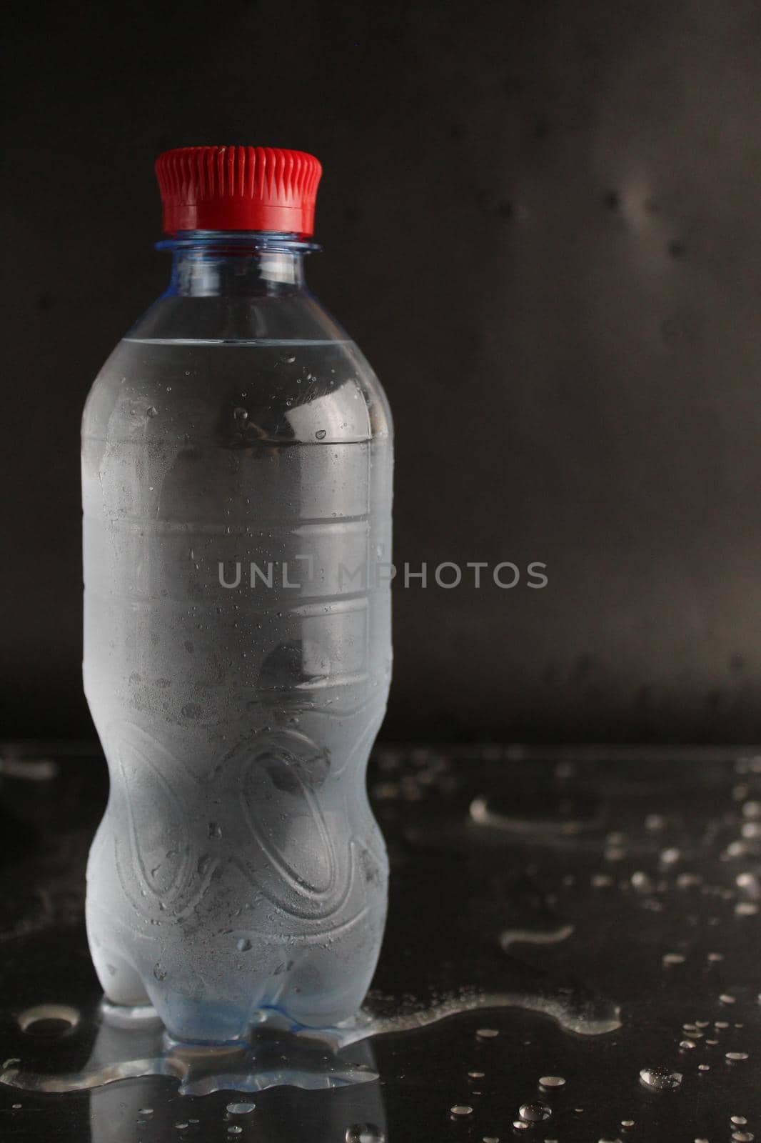 Cold water in a bottle on a black background. A bottle of water stands on a black background. Cool summer drinks.