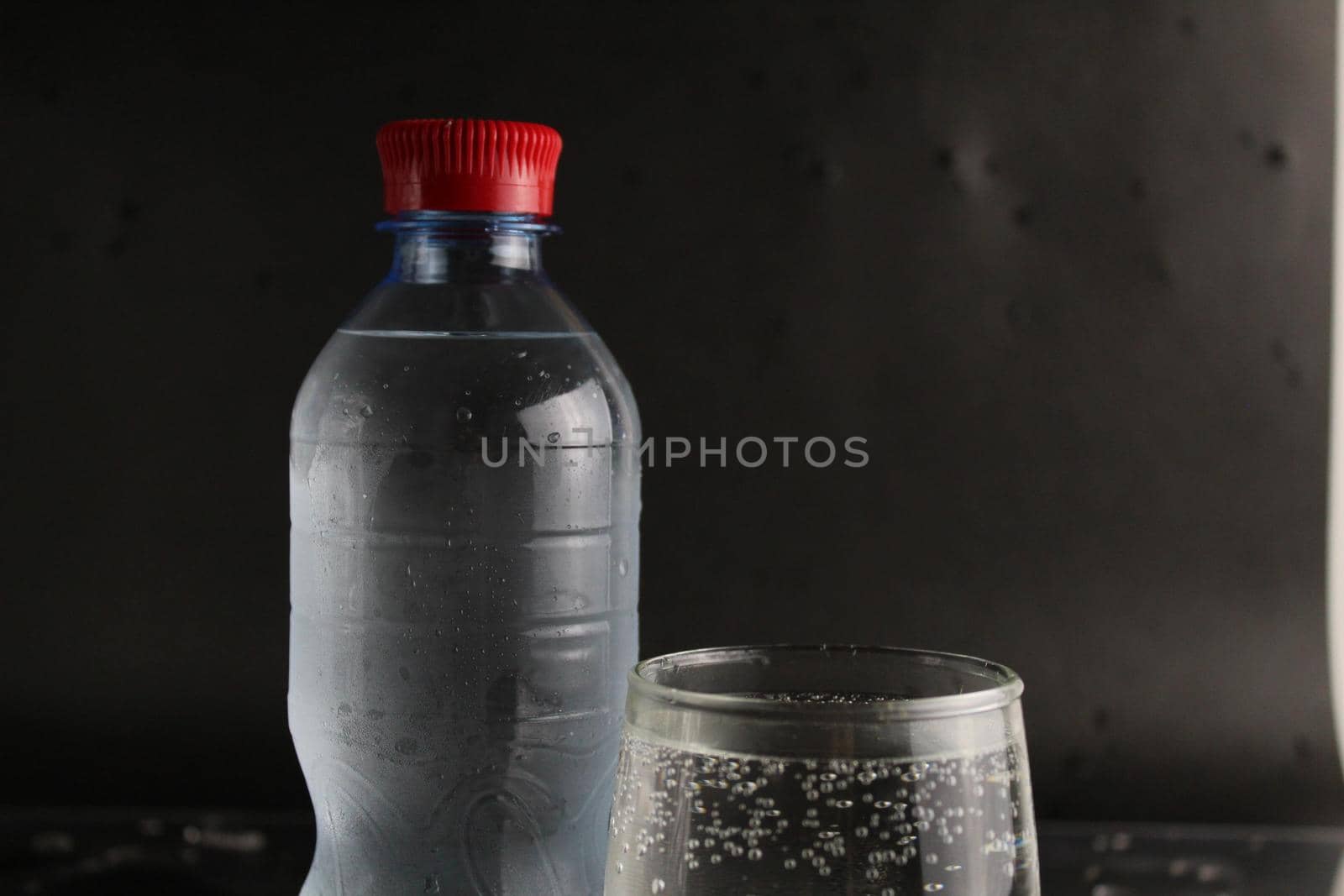 The mineral cold water in the glass and in the plastic bottle stand next to the black background with a place to insert and with a copypispe. drinking water.