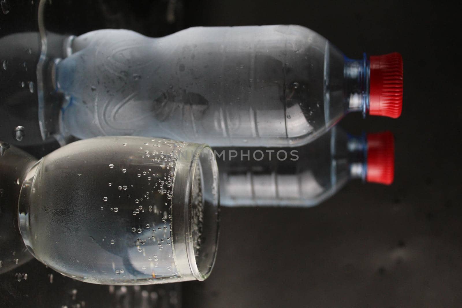 The mineral cold water in the glass and in the plastic bottle stand next to the black background with a place to insert and with a copypispe. drinking water.