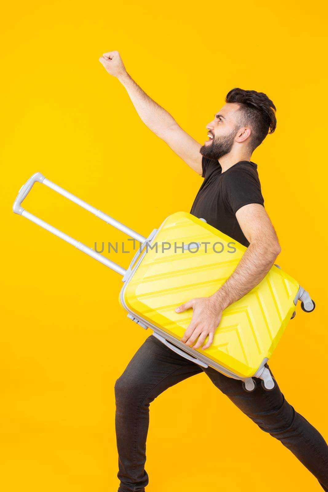 Cute pretty young arab man with a beard holding a yellow suitcase in his hands on a yellow background. Concept of travel and vacations by Satura86