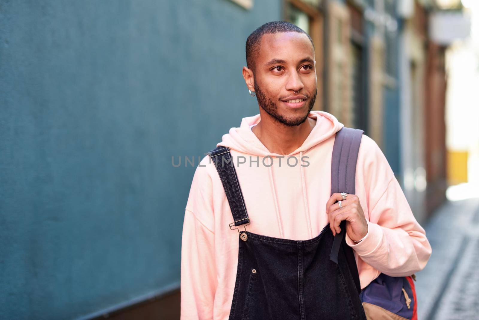 Young black man wearing casual clothes walking smiling down the street. Millennial african guy with bib pants outdoors