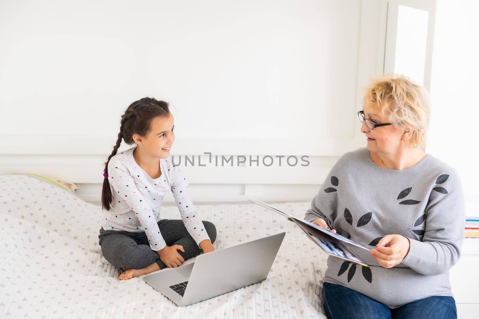 Cute and happy little girl child using laptop computer with her grandma, studying through online e-learning system.