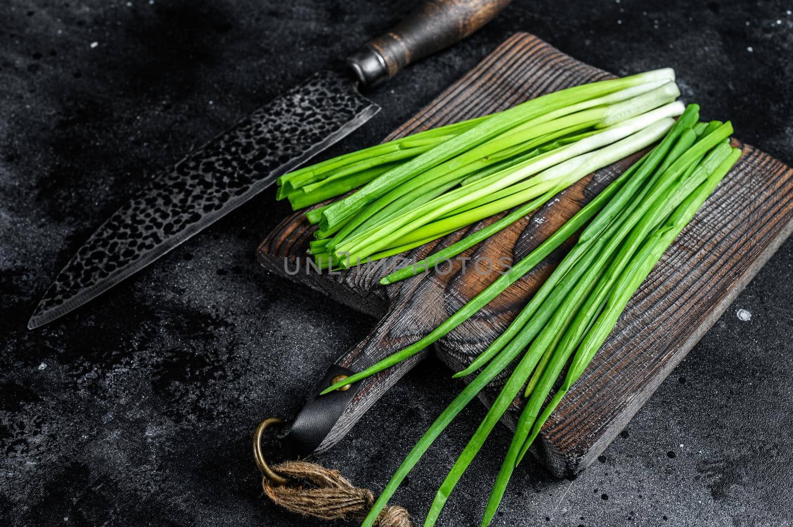 Fresh green onions on a cutting board. Black background. Top view by Composter