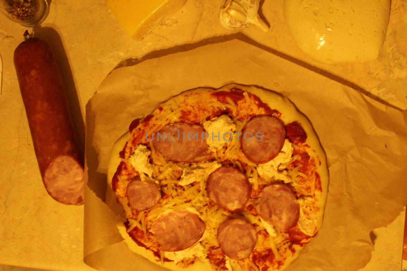 pizza with ham sausage. Homemade pizza meals lie on parchment next to the sausage. Top view.