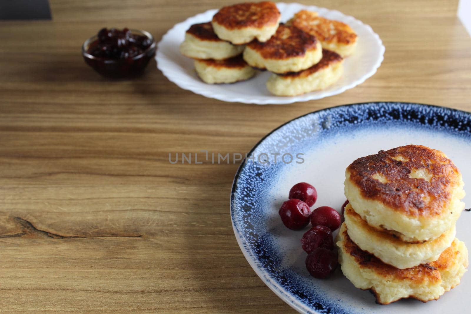 Three pancake cheesecakes lie a stack of slides on top of each other on a plate on a table with cherry cherry jam sauce. View from the side. Breakfast is Russian Ukrainian. Dishes and cottage cheese. Place for text and with copyspace.