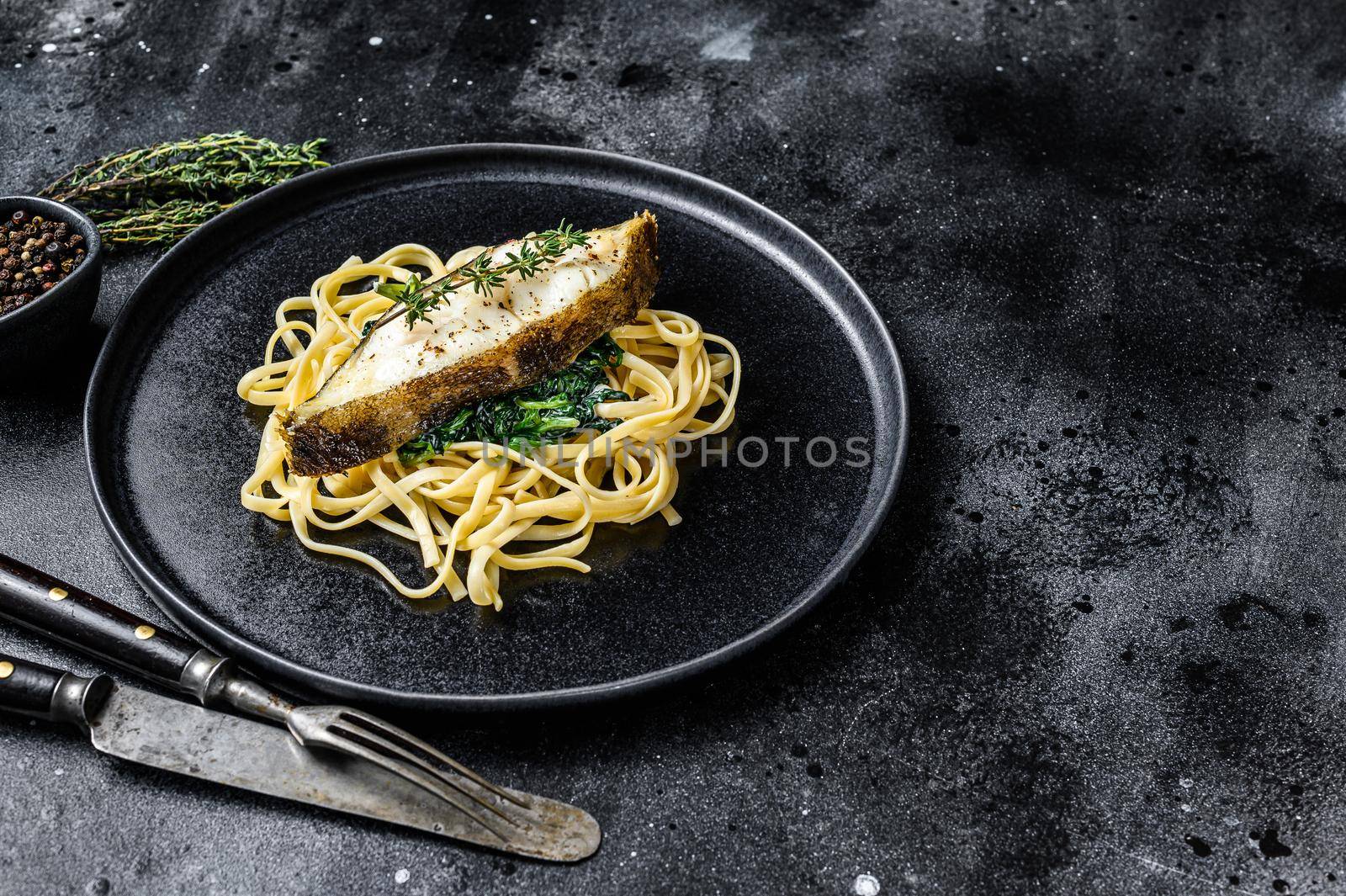 Spaghetti pasta with Halibut fish steak and spinach. Black background. Top view. Copy space by Composter