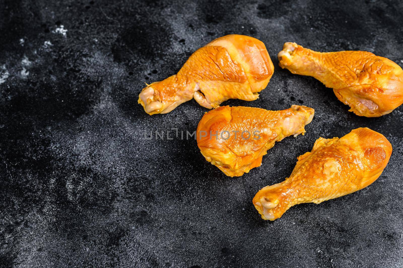 Spicy Smoked chicken leg drumsticks on a kitchen table. Black background. Top view. Copy space by Composter