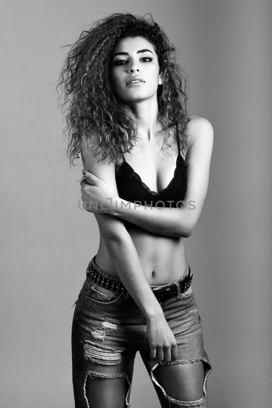 Beautiful young woman with black curly hairstyle. Girl wearing black bra and blue jeans.