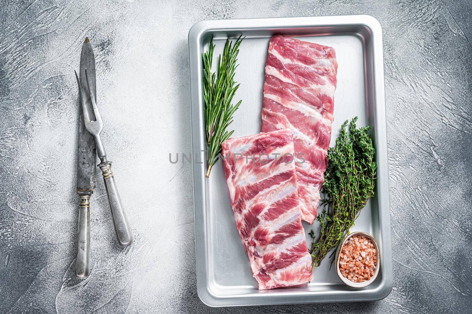 Raw pork spare ribs in kitchen tray with herbs. White background. Top view.