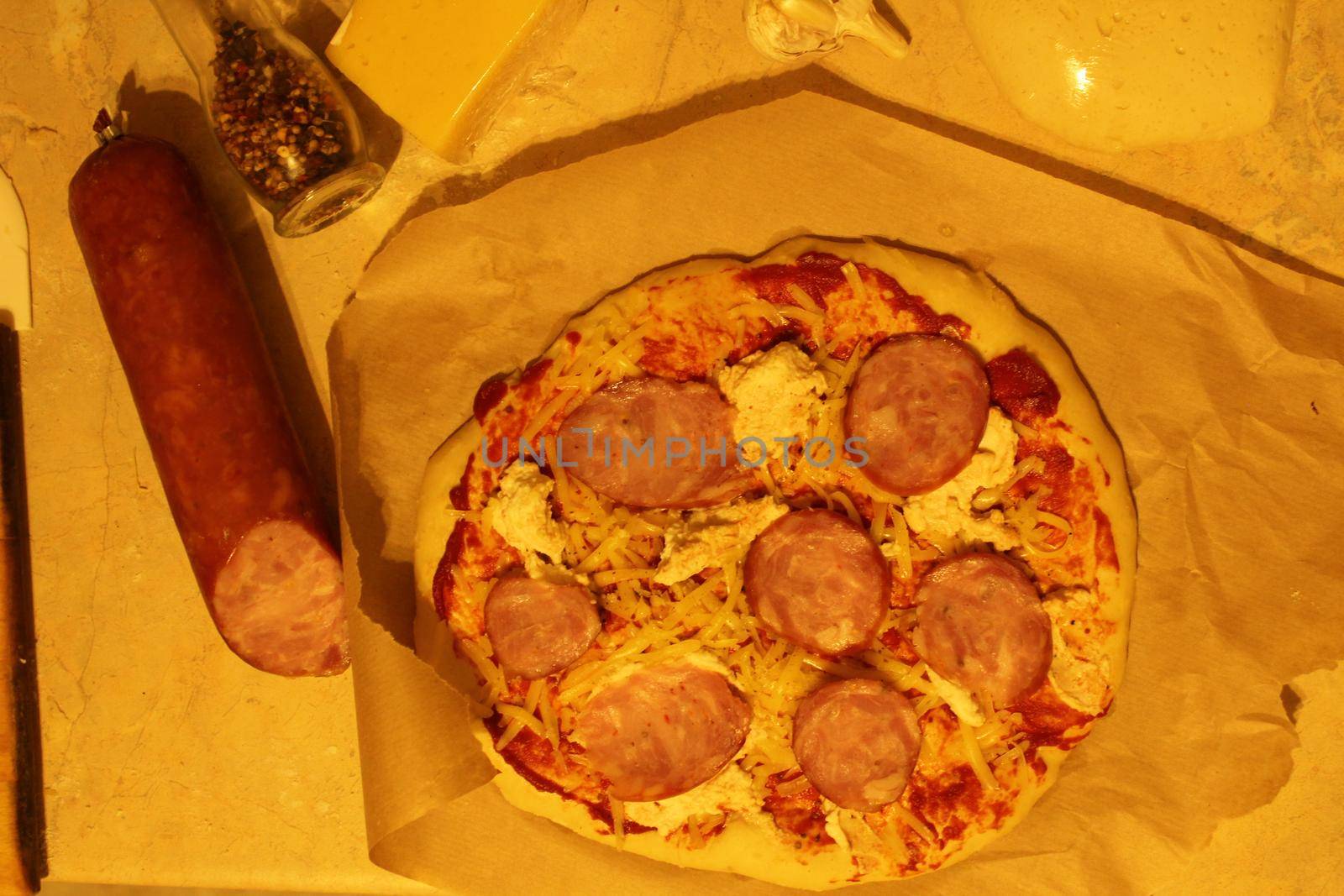 pizza with ham sausage. Homemade pizza meals lie on parchment next to the sausage. Top view.