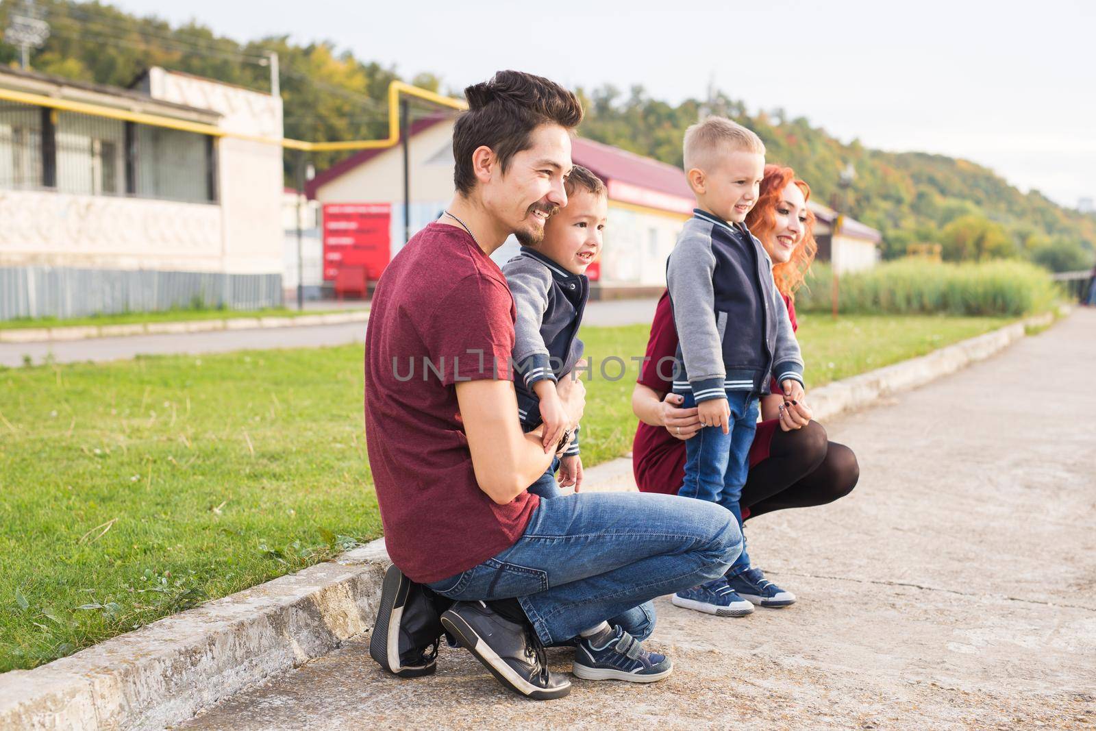 Parenthood, childhood and family concept - Parents and two male children walking at the park and looking on something.