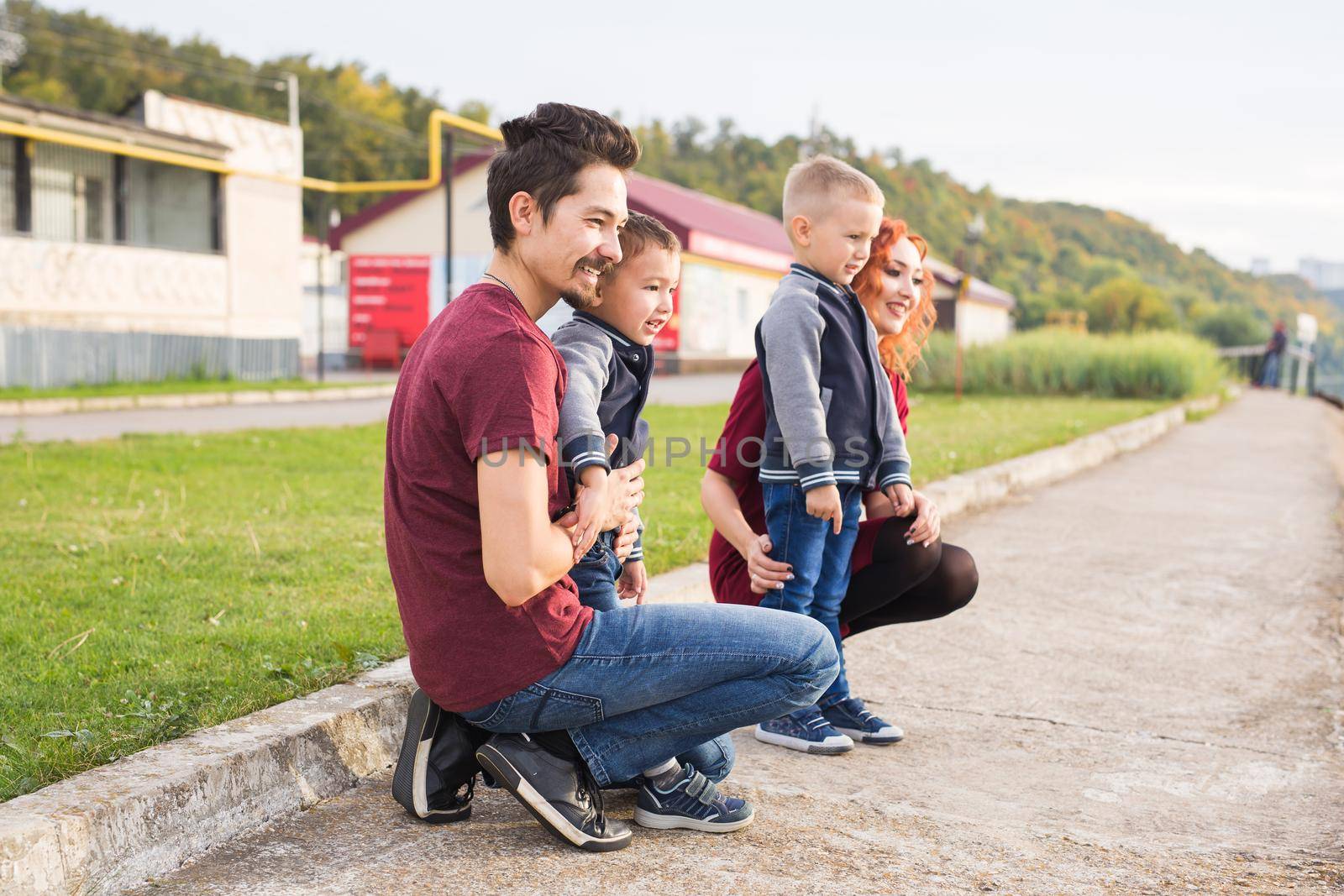 Parenthood, childhood and family concept - Parents and two male children walking at the park and looking on something.