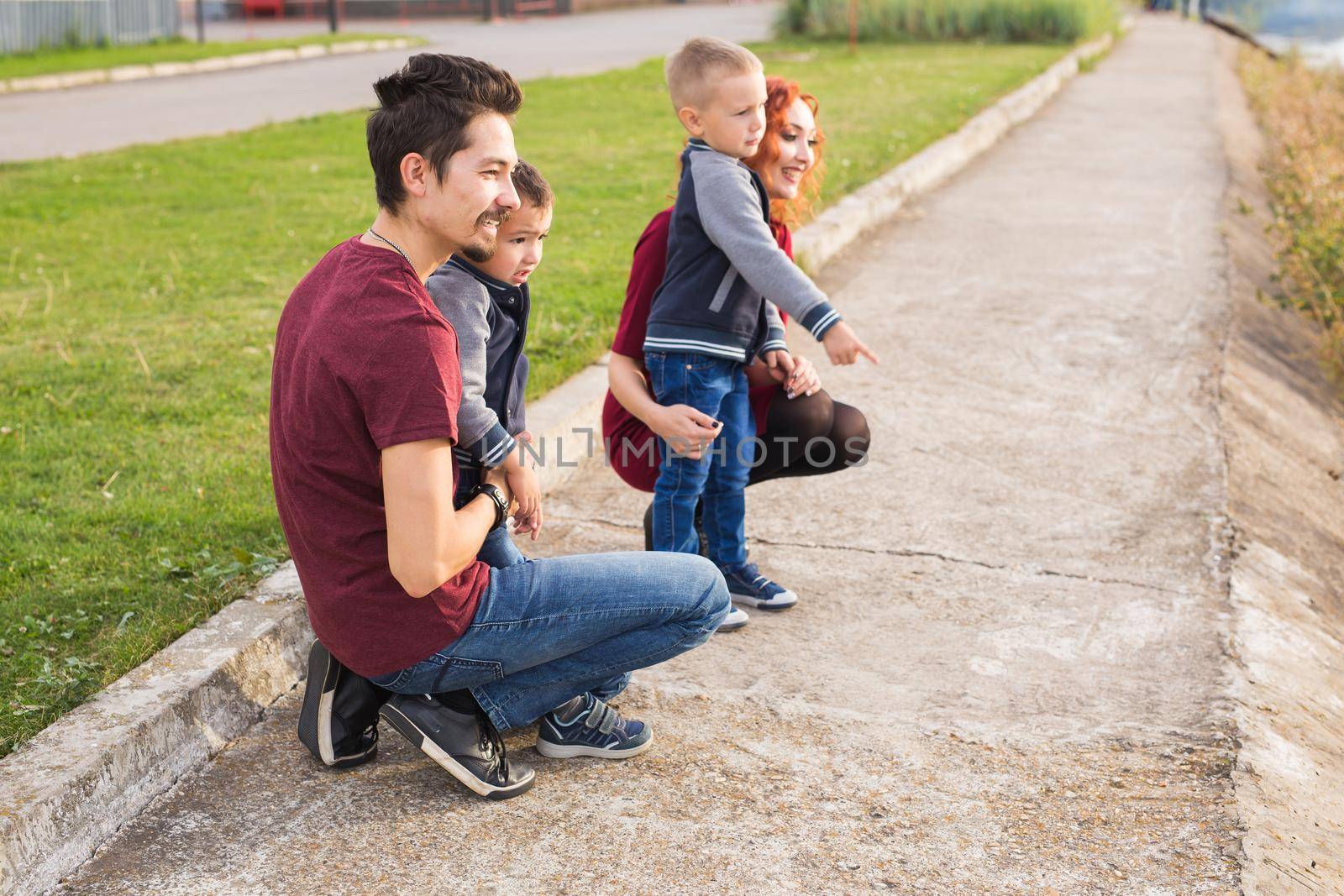 Parenthood, childhood and family concept - Parents and two male children walking at the park and looking on something.