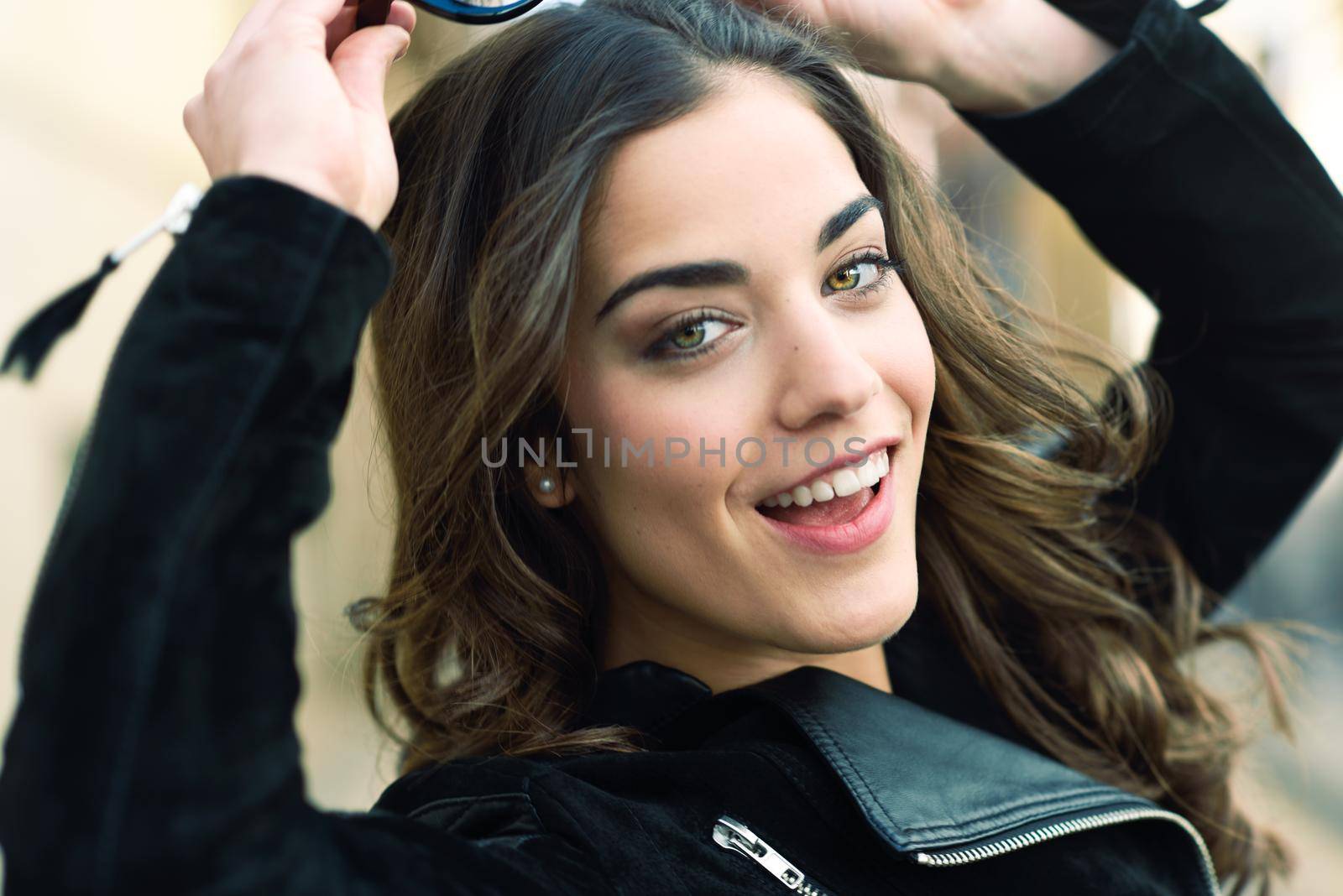 Portrait of young woman smiling in urban background wearing casual clothes with modern sunglasses. Girl with long curly hair