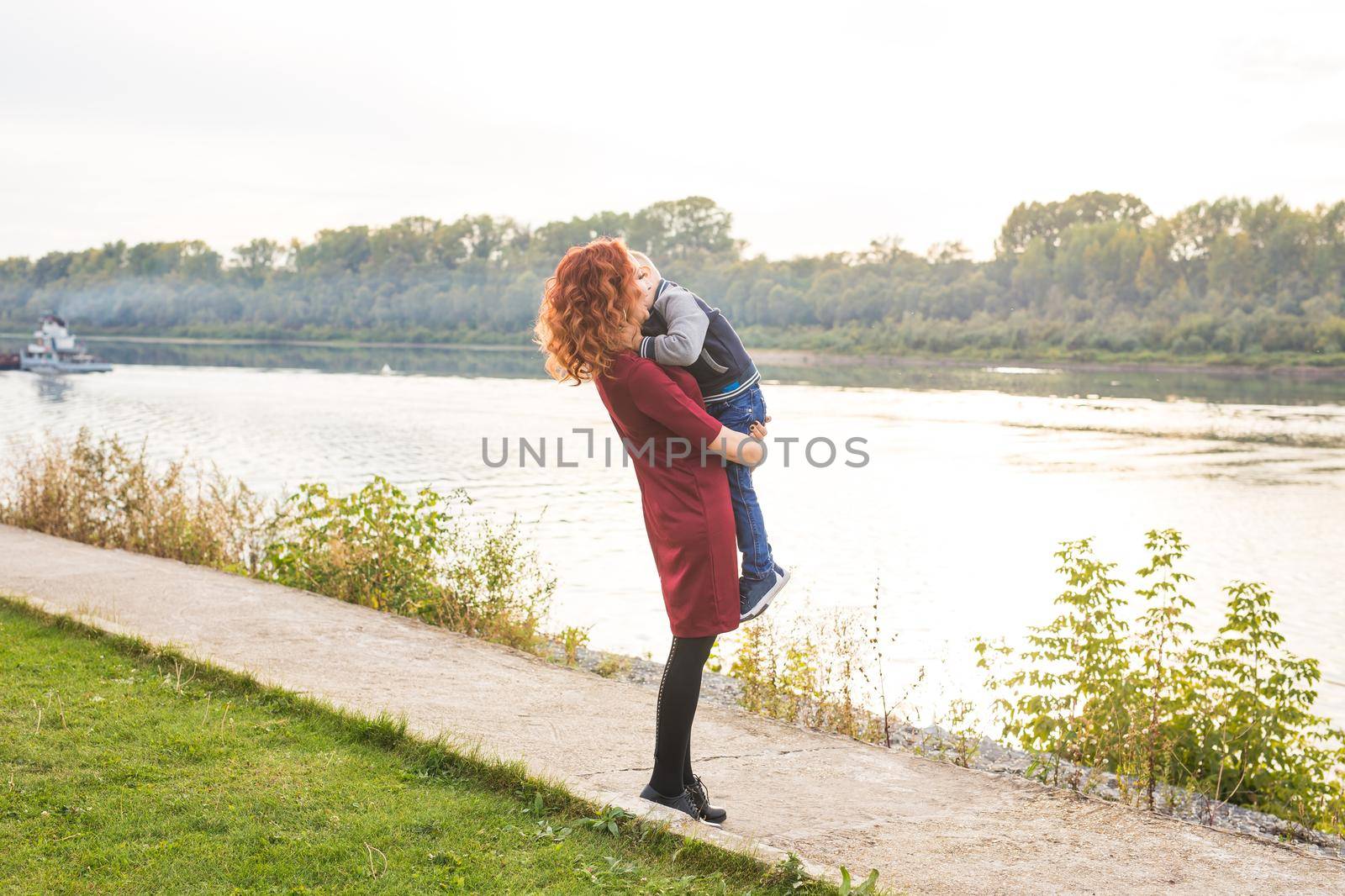 Motherhood and children concept - young mother with son in her arms near the river by Satura86