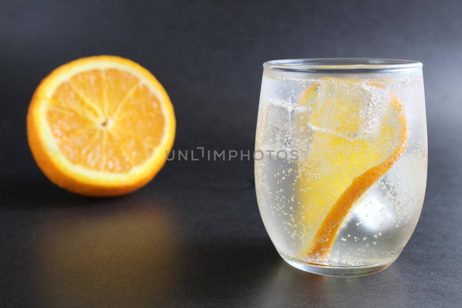 lemonade with orange and ice in a glass on a black background next to lies ice and orange. Summer drink on a black background.