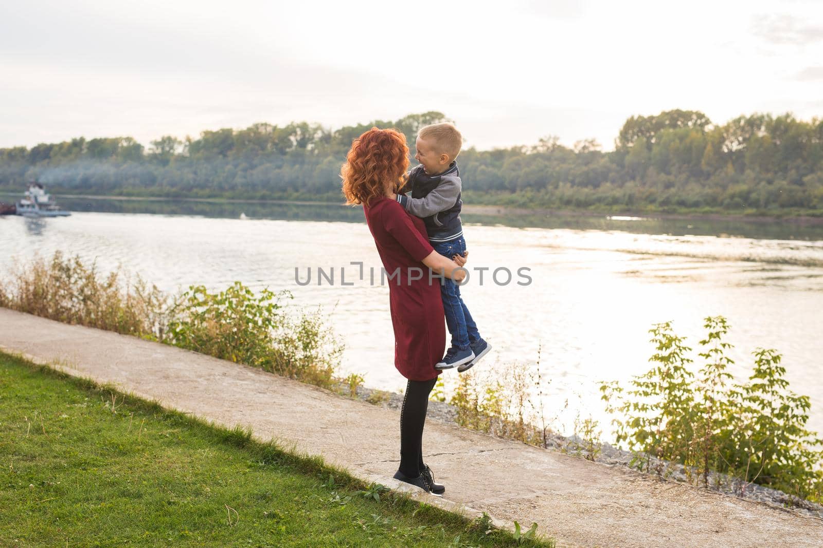 Motherhood and children concept - young mother with son in her arms near the river.