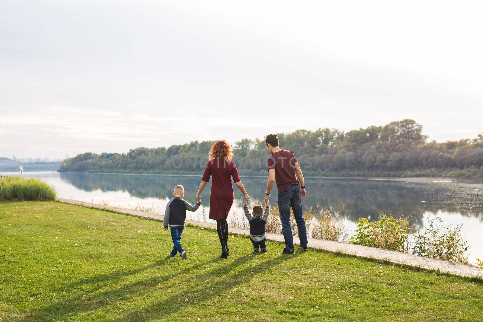 Parenthood and nature concept -Family of mother and father with two boys twins kids in a park at summer by a river at sunny day.