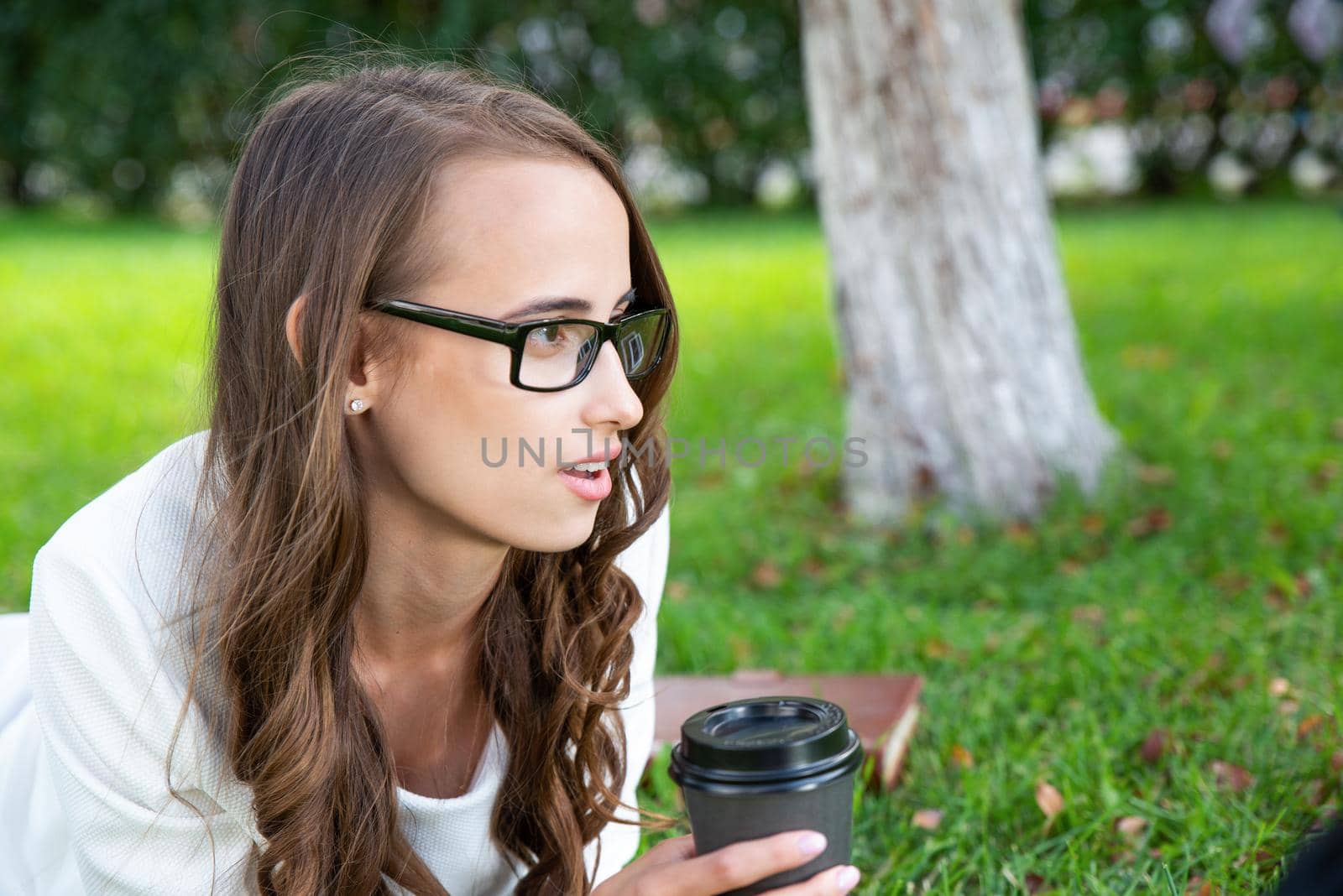portrait of a young attractive woman in the park with a paper glass of coffee. Rest in the park
