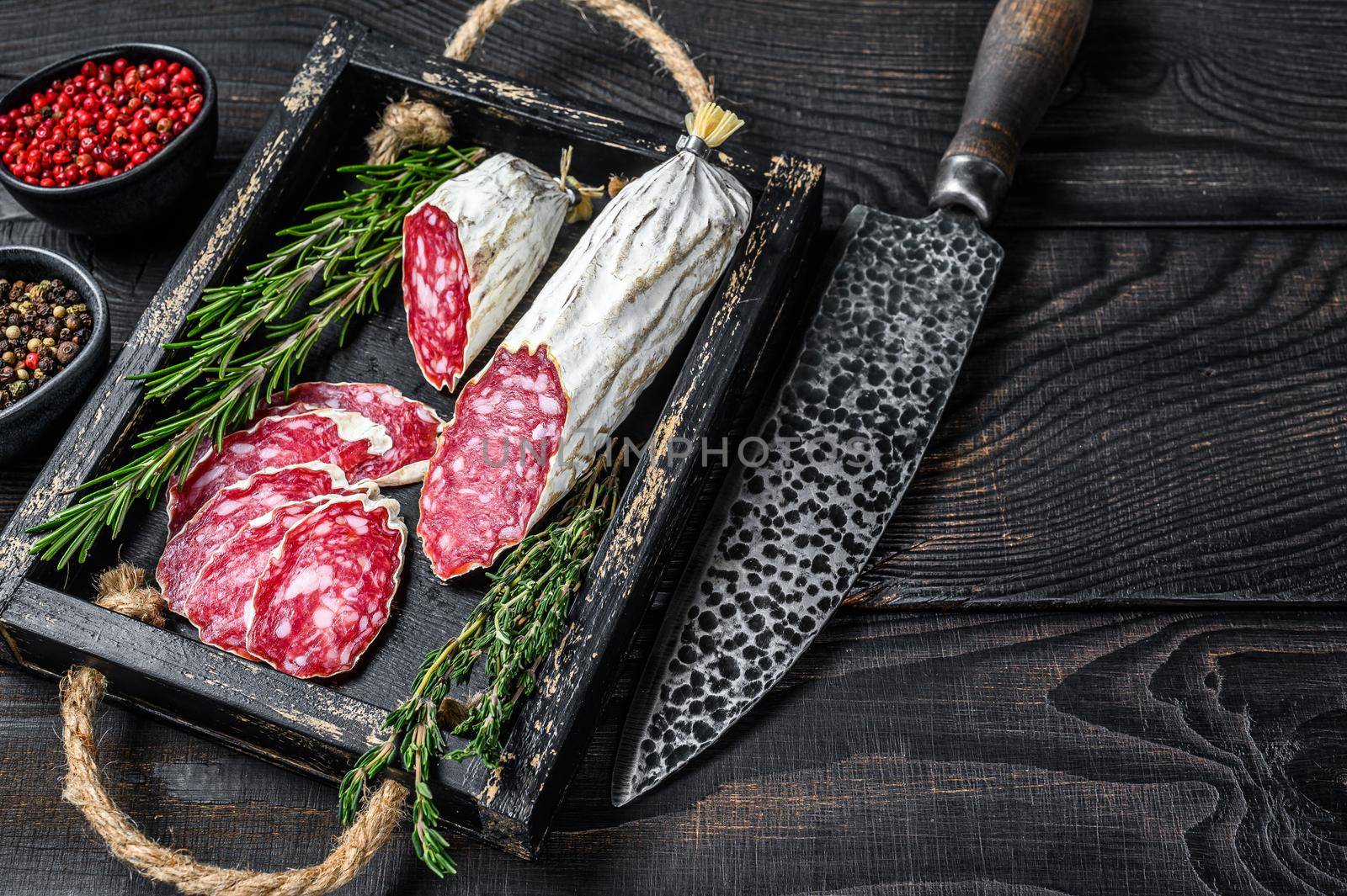 Slices of dry cured salchichon salami in a wooden tray. Black wooden background. Top view. Copy space by Composter