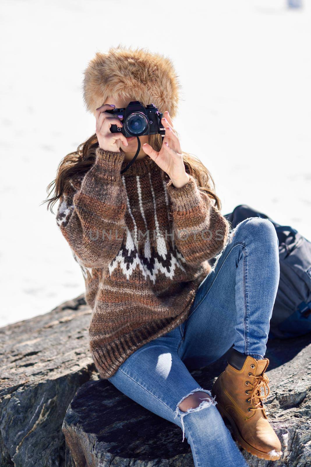 Young woman taking photographs in the snowy mountains in winter, in Sierra Nevada, Granada, Spain. Female wearing winter clothes.