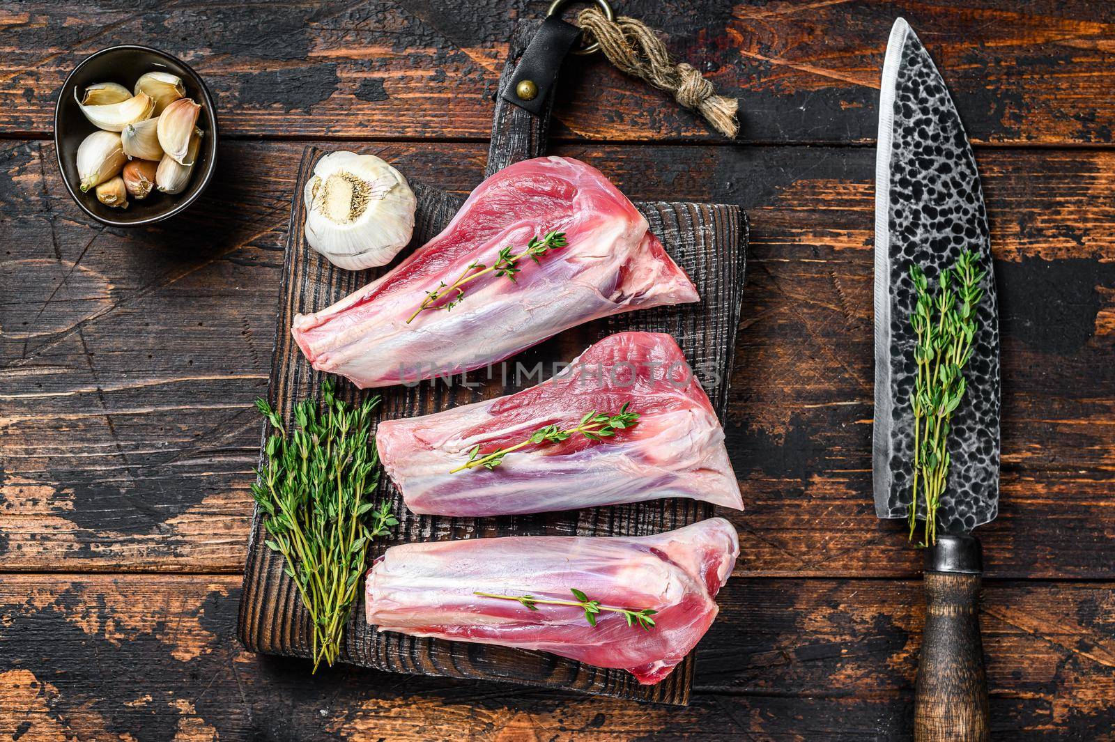 Raw lamb shanks meat on a cutting board with herbs. Dark wooden background. Top view by Composter