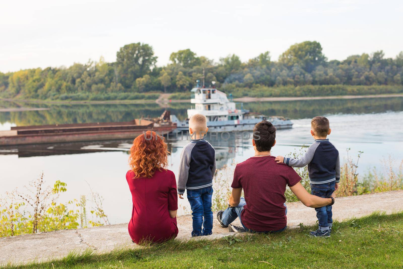 Parenthood, childhood and nature concept - Family sitting on the green ground and looking at small boat by Satura86