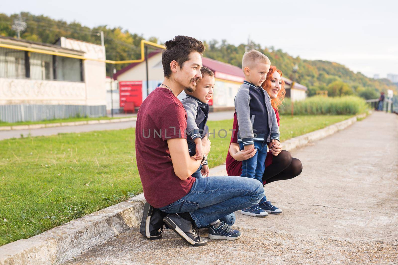 Parenthood, childhood and family concept - Parents and two male children walking at the park and looking on something.