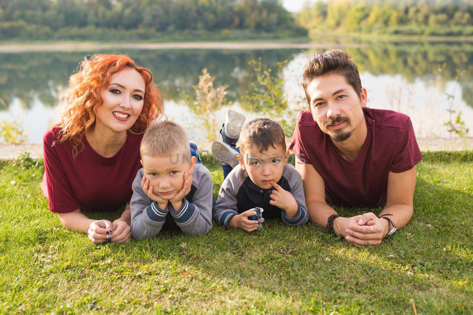 Childhood and nature concept - Family with little sons sitting on the green grass.