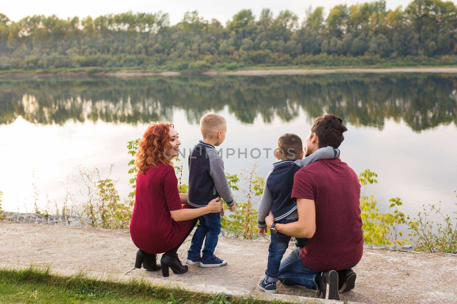 Parenthood, childhood and family concept - Parents and two male children walking at the park and looking on something.