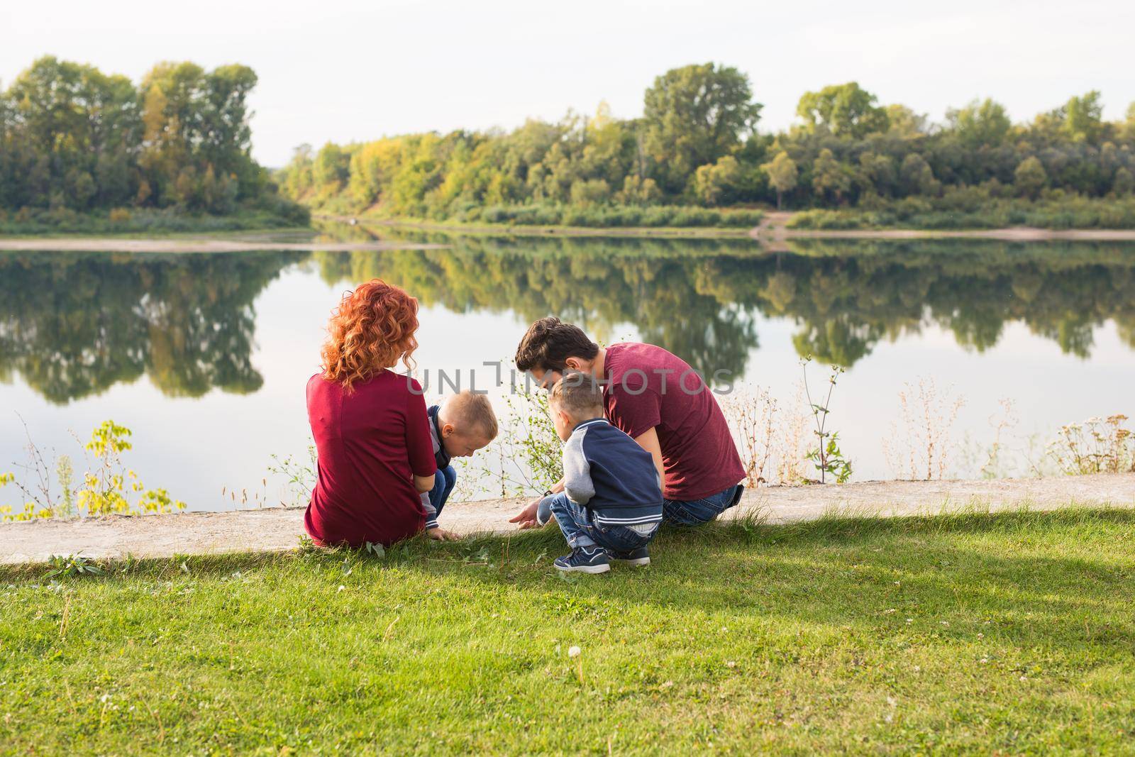 Childhood and nature concept - Family with little sons sitting on the green grass.