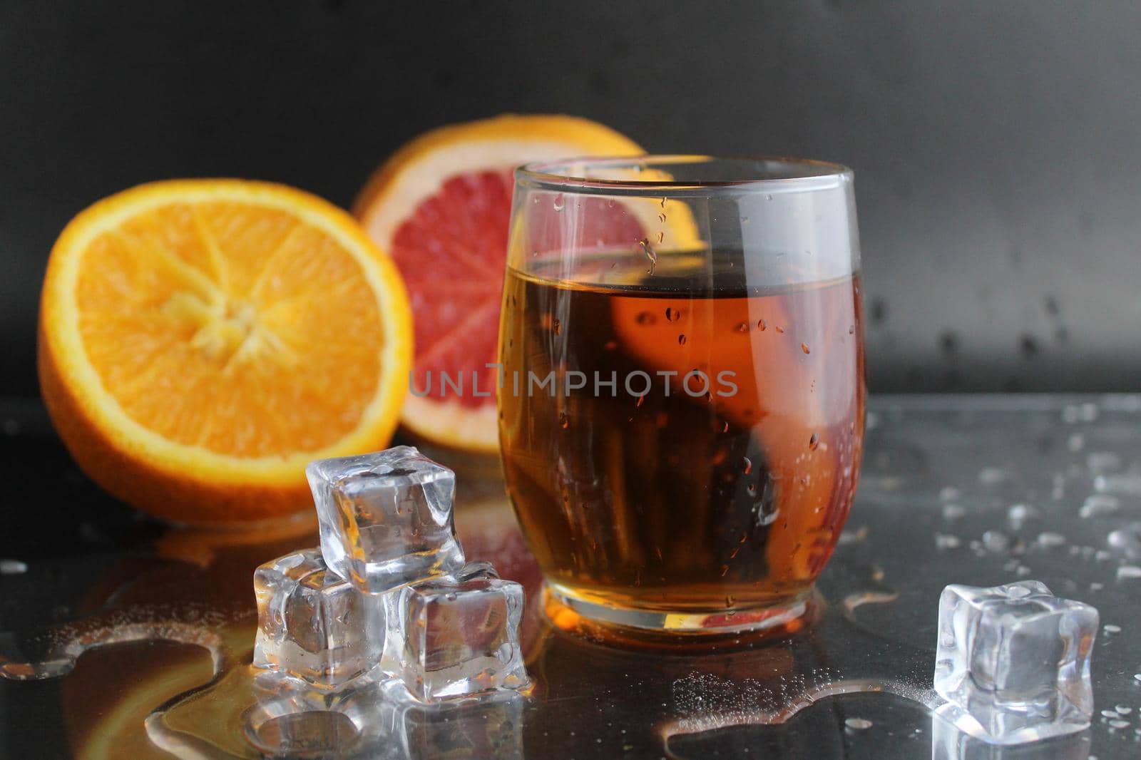 Apple citrus dark juice in a glass next to lies citrus orange grapefruit ice on a black background. Refreshing drinks, summer, soft drinks.