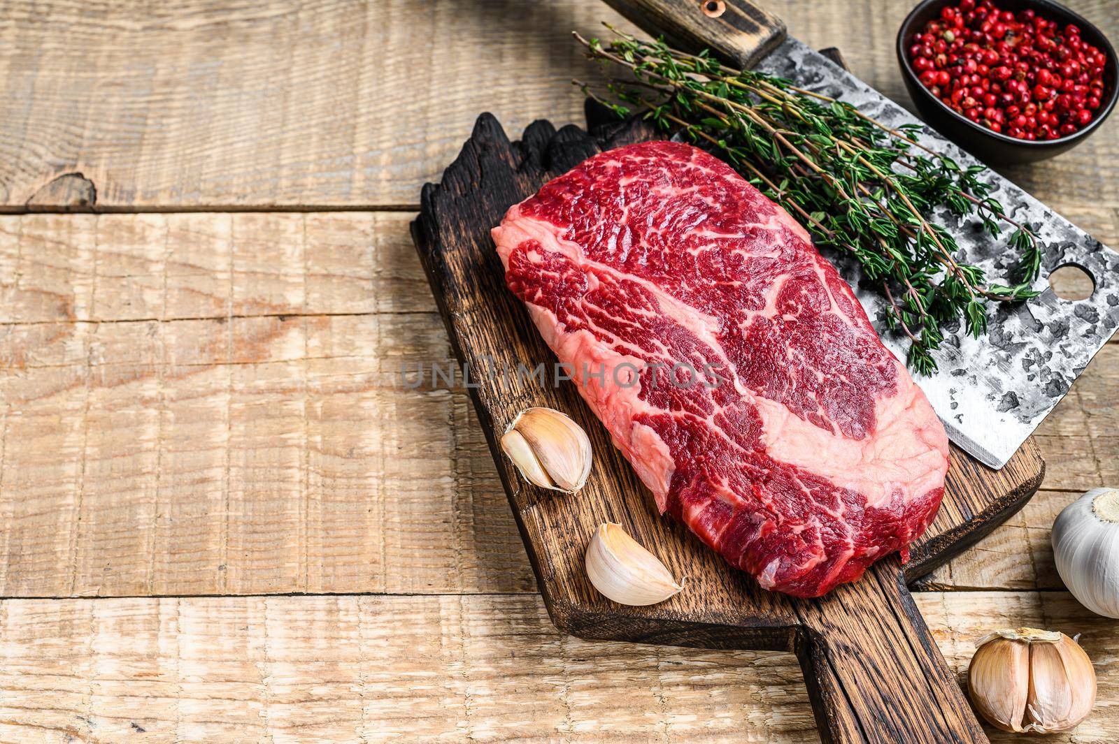 Prime rib eye raw beef meat steak on a butcher wooden cutting board with cleaver. wooden background. Top view. Copy space.