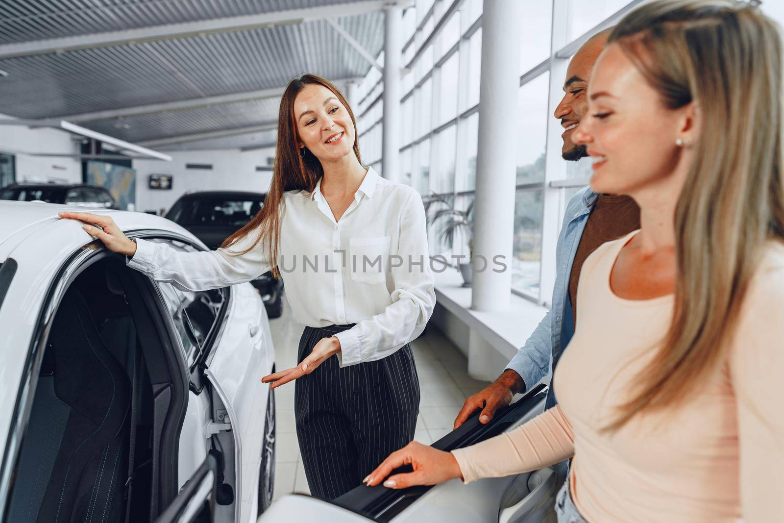 Woman car dealer explaining to buyers features of their new car by Fabrikasimf