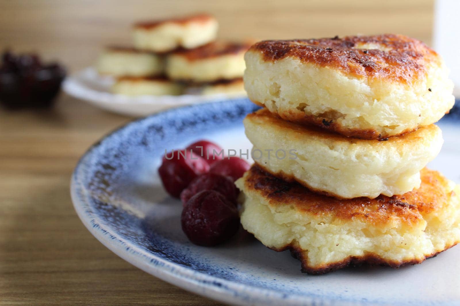Three pancake cheesecakes lie a stack of slides on top of each other on a plate on a table with cherry cherry jam sauce. View from the side. Breakfast is Russian Ukrainian. Dishes and cottage cheese. Place for text and with copyspace by Shoba