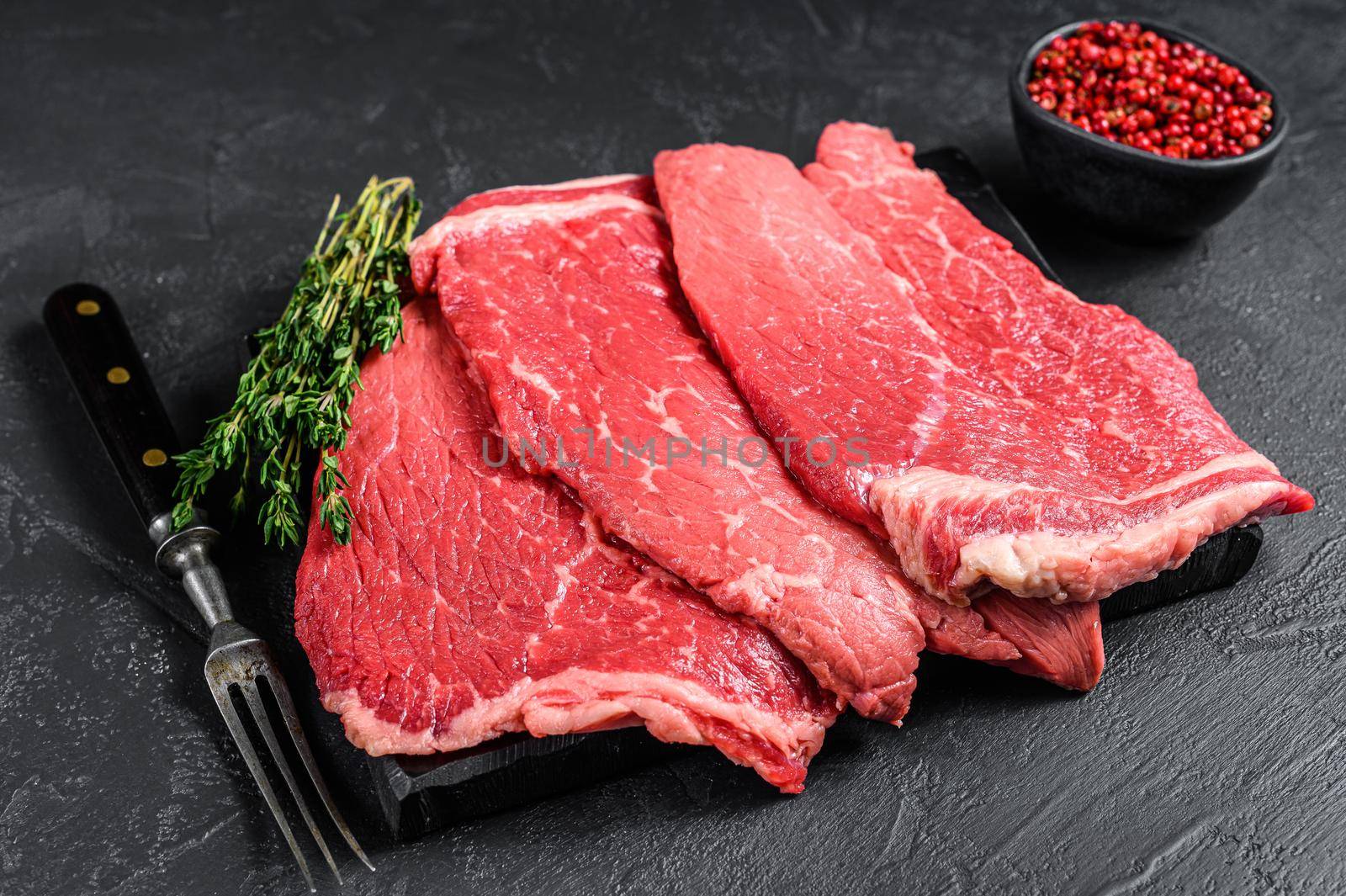 Raw beef meat round steak on a marble board. Black background. Top view by Composter