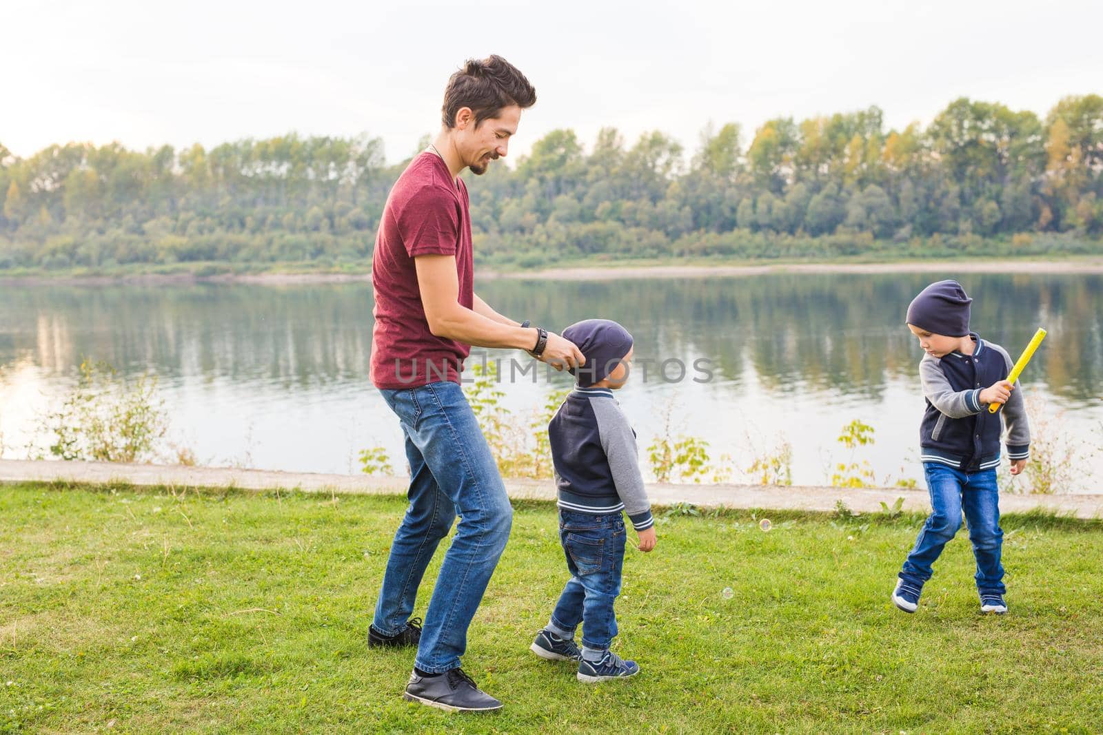 Childhood, family concept - father playing with two sons near the lake.