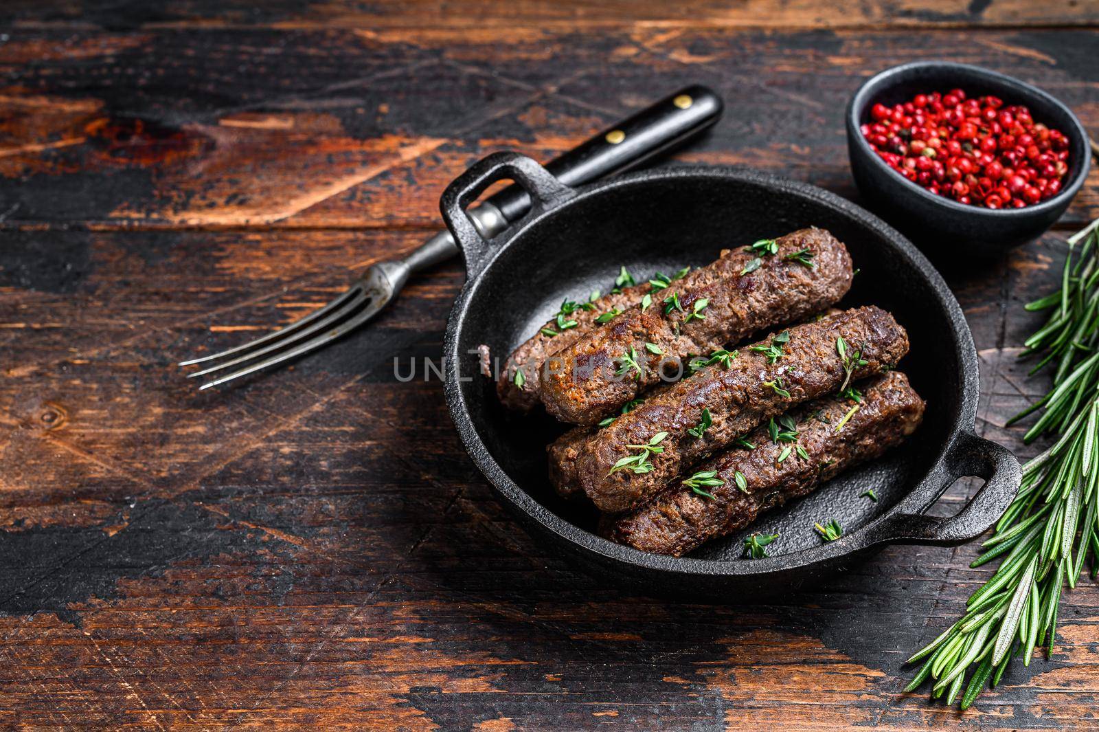 Grilled mince meat sausages in a pan. Dark wooden background. Top view. Copy space.