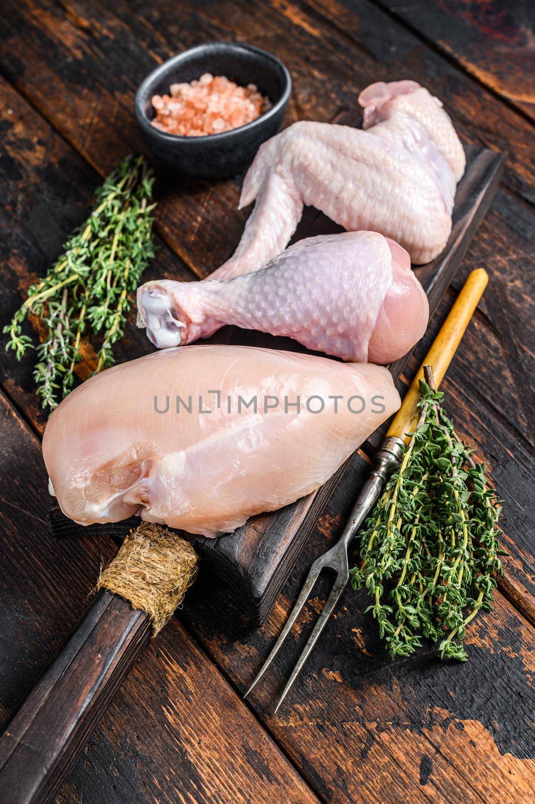 Raw chicken portions for cooking and barbecuing with skinless breasts, drumstick and wings. Dark wooden background. Top view.