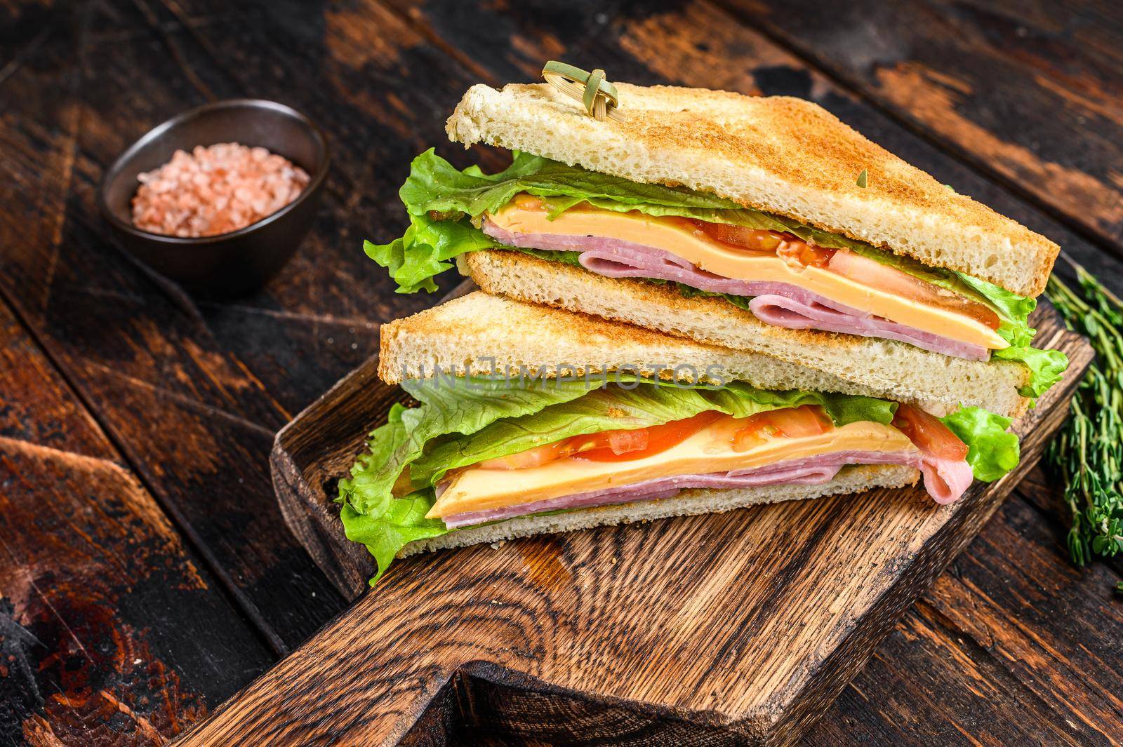 Turkey Ham Club sandwiches with cheese, tomatoes and lettuce on a wooden cutting board. Dark wooden background. Top view.