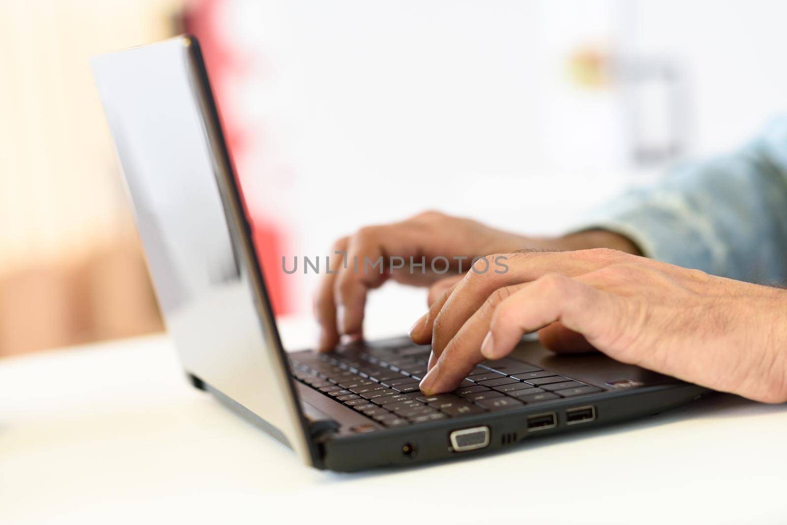 Hands of a man typing with a laptop computer in a coffee bar.