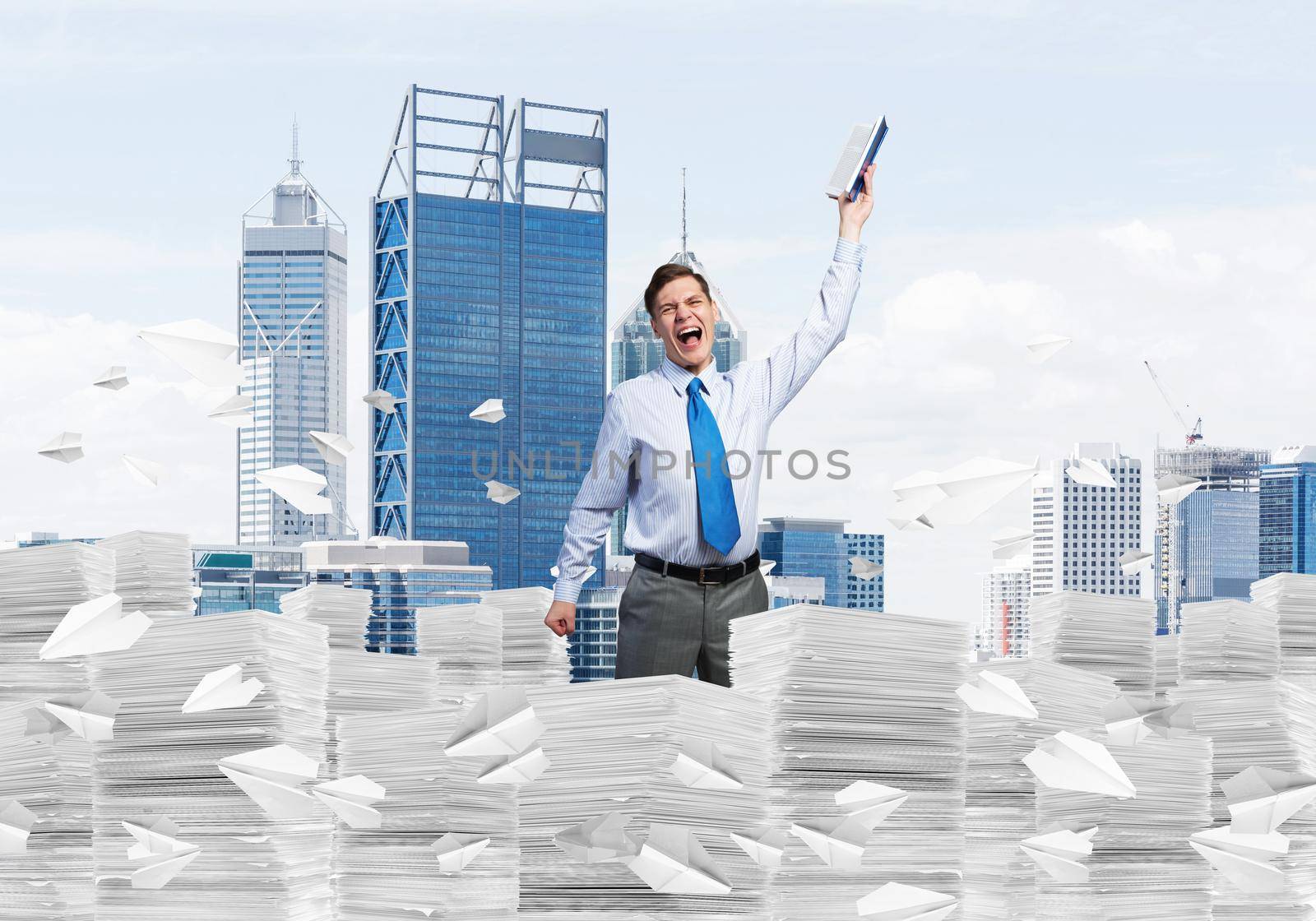 Businessman keeping hand with book up while standing among flying paper planes with cityscape on background. Mixed media.